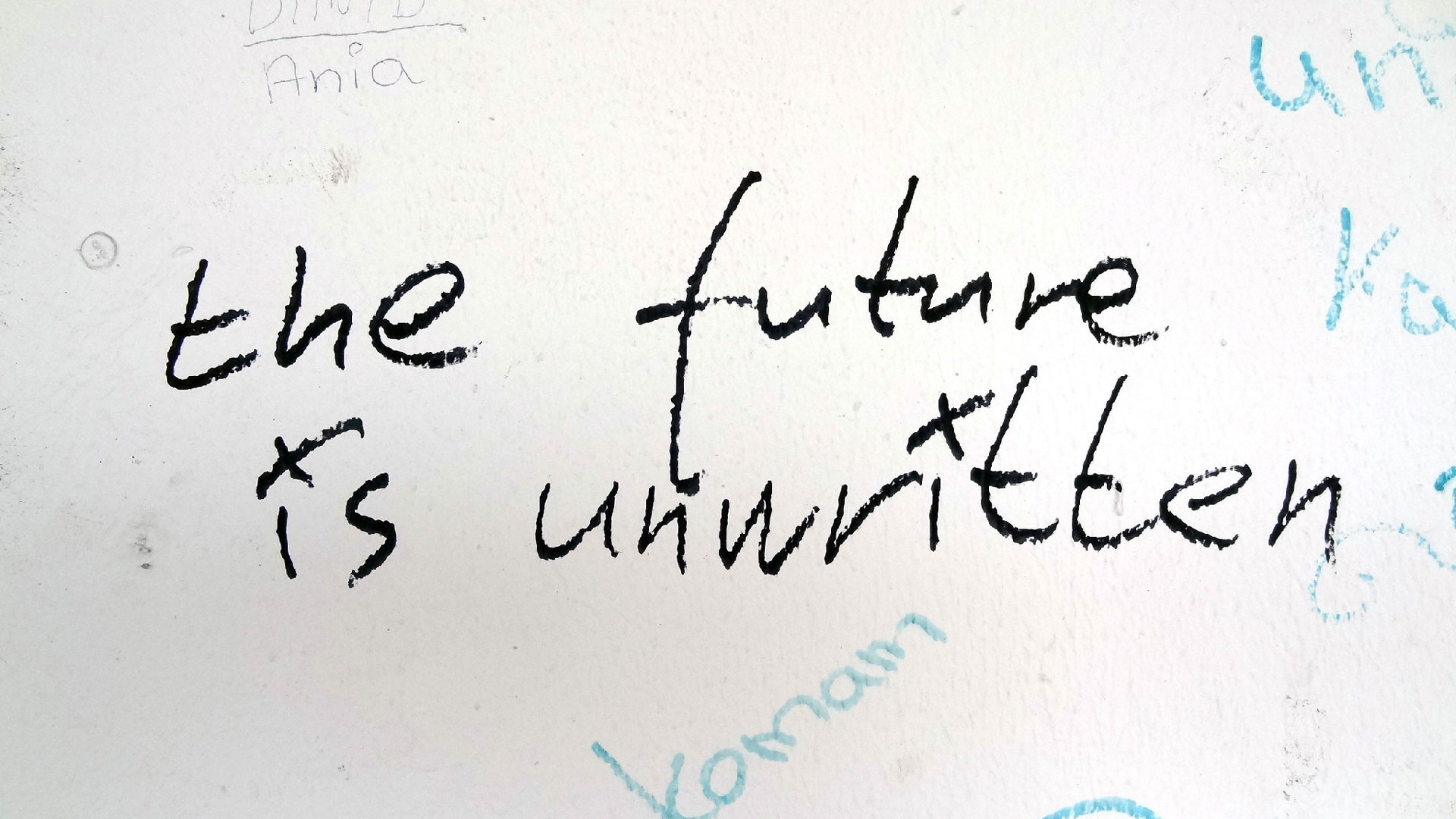 Graffiti-style handwritten message on a white wall that reads 'the future is unwritten'.