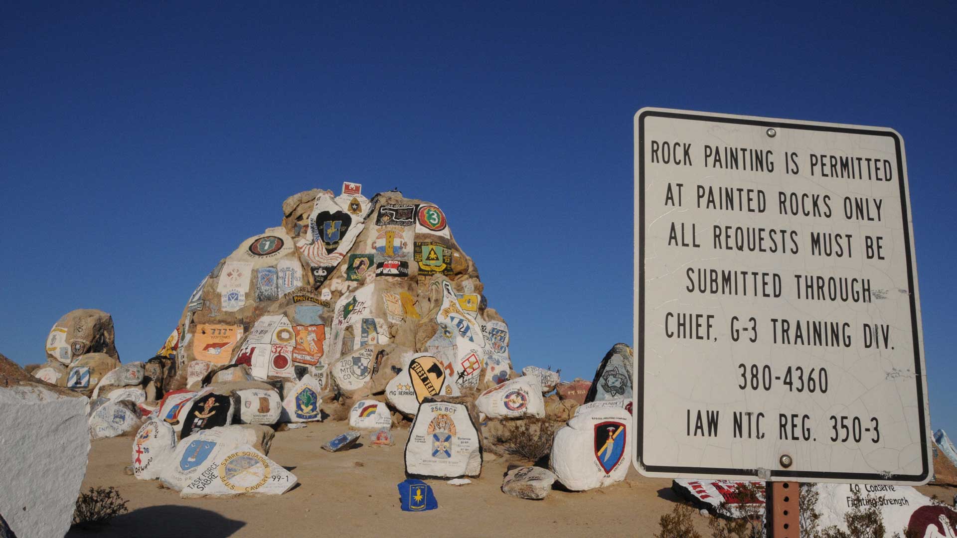 Military unit insignia painted on rocks at Fort Irwin National Training Center with regulatory sign for Painted Rocks area