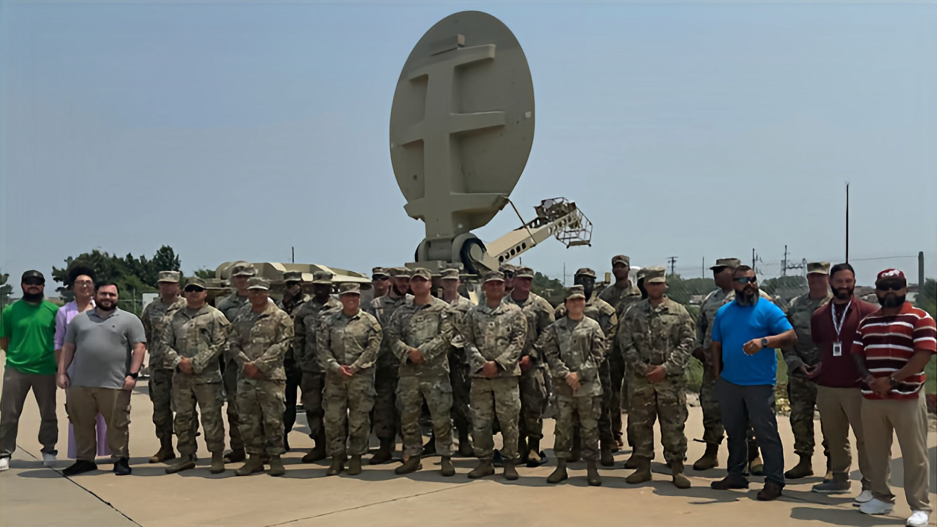 Group photo of soldiers and civilians in front of a military satellite dish.