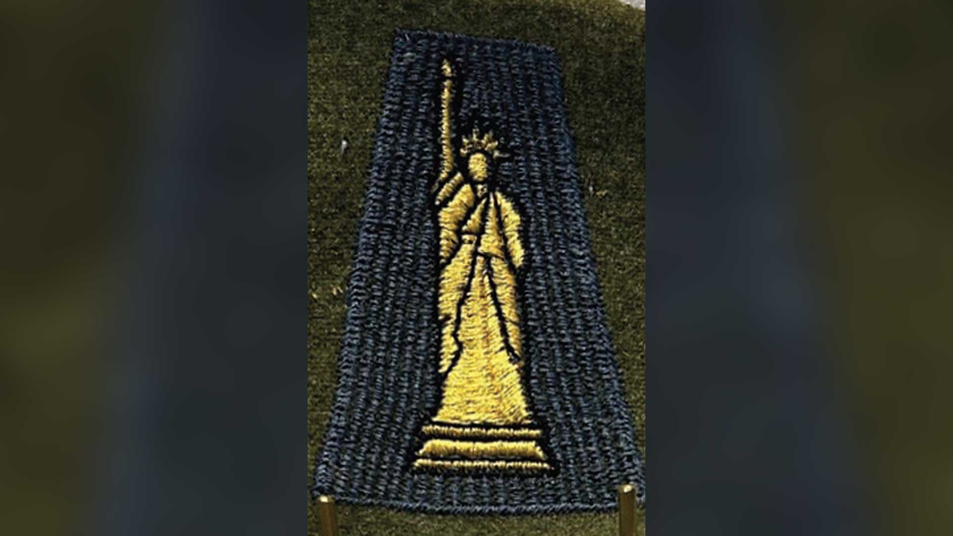 A close-up photograph of a World War I military shoulder sleeve insignia patch from the 77th Division. The embroidered patch displays the Statue of Liberty in golden-yellow thread against a navy blue fabric background.