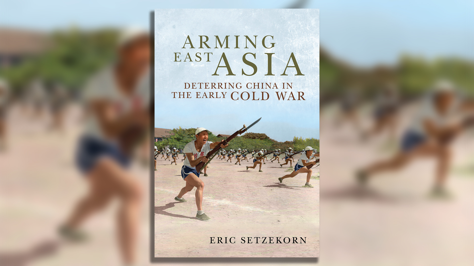  Book cover of 'Arming East Asia: Deterring China in the Early Cold War' by Eric Setzekorn. The cover features a historical photograph showing military personnel in white t-shirts and dark shorts conducting bayonet training exercises on a dirt field. The soldiers are running forward with rifles equipped with bayonets, wearing military helmets. The scene appears to be from the Cold War era, with buildings and hills visible in the background. The title appears in large olive-green text at the top, with the subtitle in smaller red text below it, and the author's name in black text at the bottom.