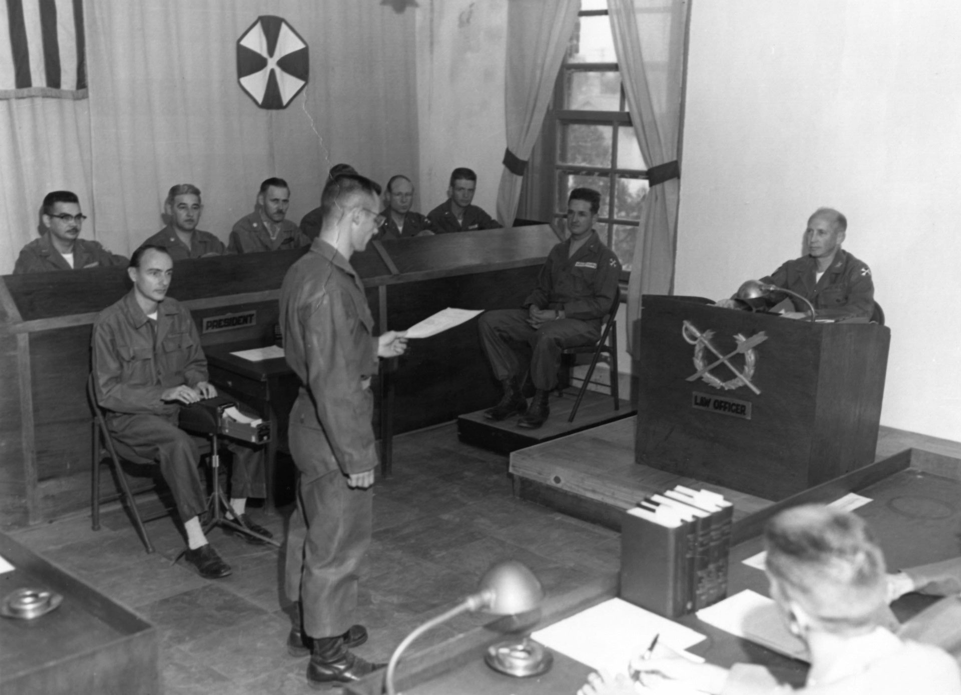 Black and white photo of a military courtroom with uniformed personnel during a legal proceeding.