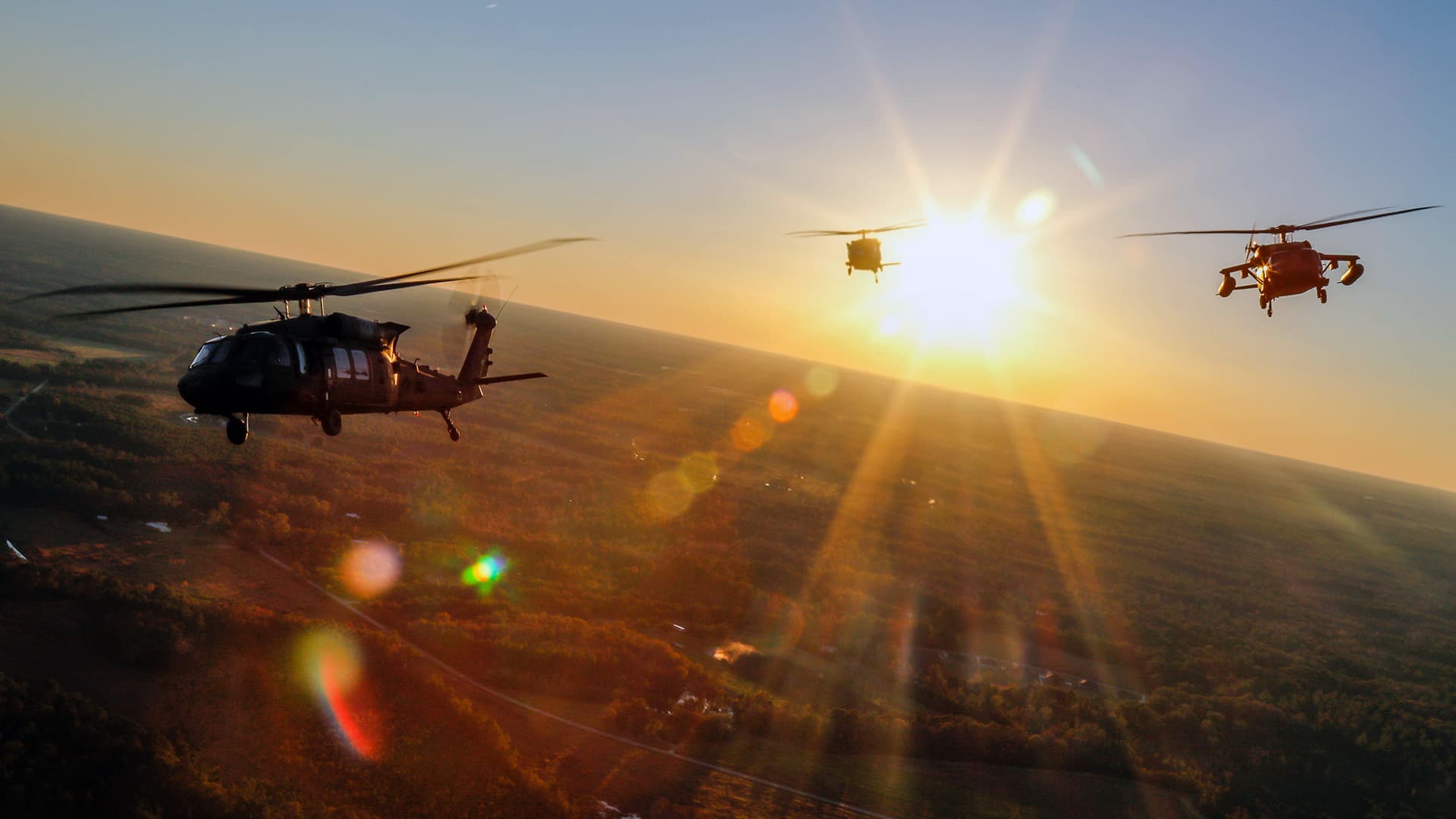 Three helicopters flying in formation as the sunrises.