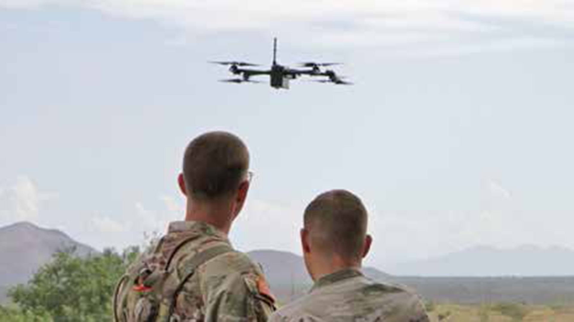 Picture of two soldiers looking towards a small unmanned aircraft system that is flying