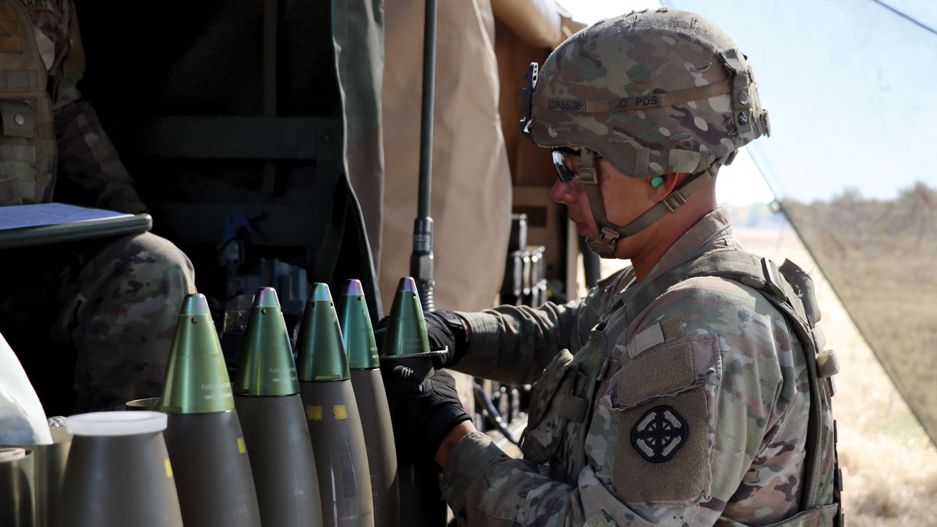 US soldier in camouflage handling green-fuzed mortar rounds inside a vehicle