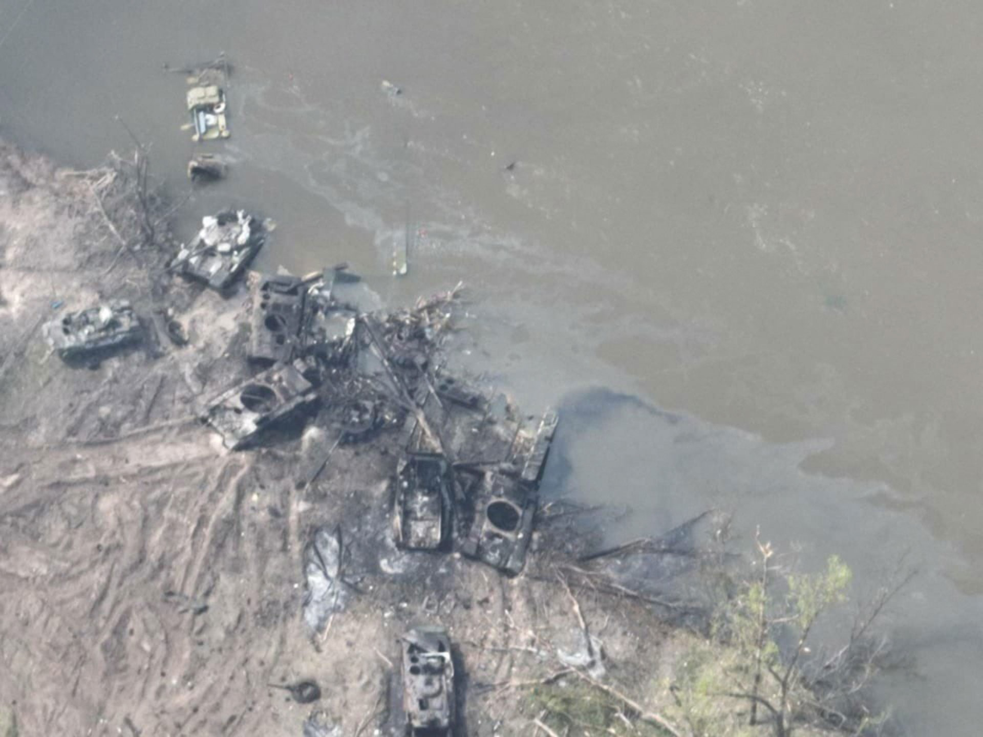 Destroyed armored vehicles and tanks scattered near a riverbank.