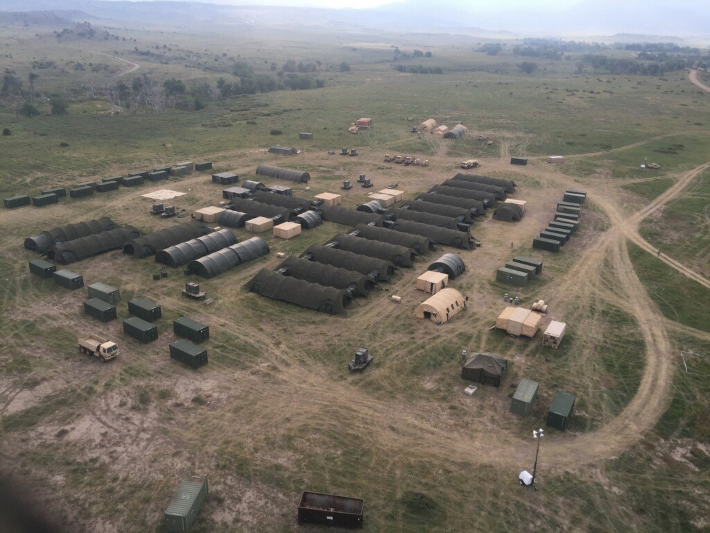 An aerial view of a large military field hospital setup with tents and containers.