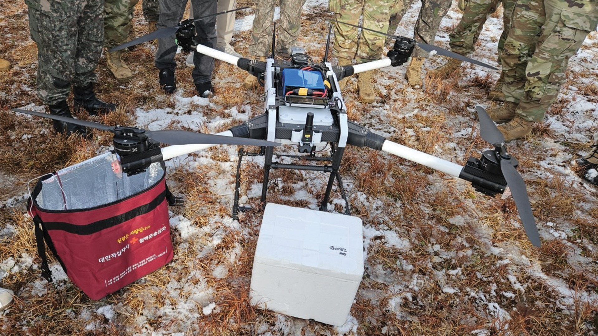 Military personnel in camouflage uniforms setting up or operating field medical equipment on muddy ground. The setup includes what appears to be portable medical devices, containers, and various pieces of field medical gear arranged on the ground, likely part of a field medical training exercise or operation.
