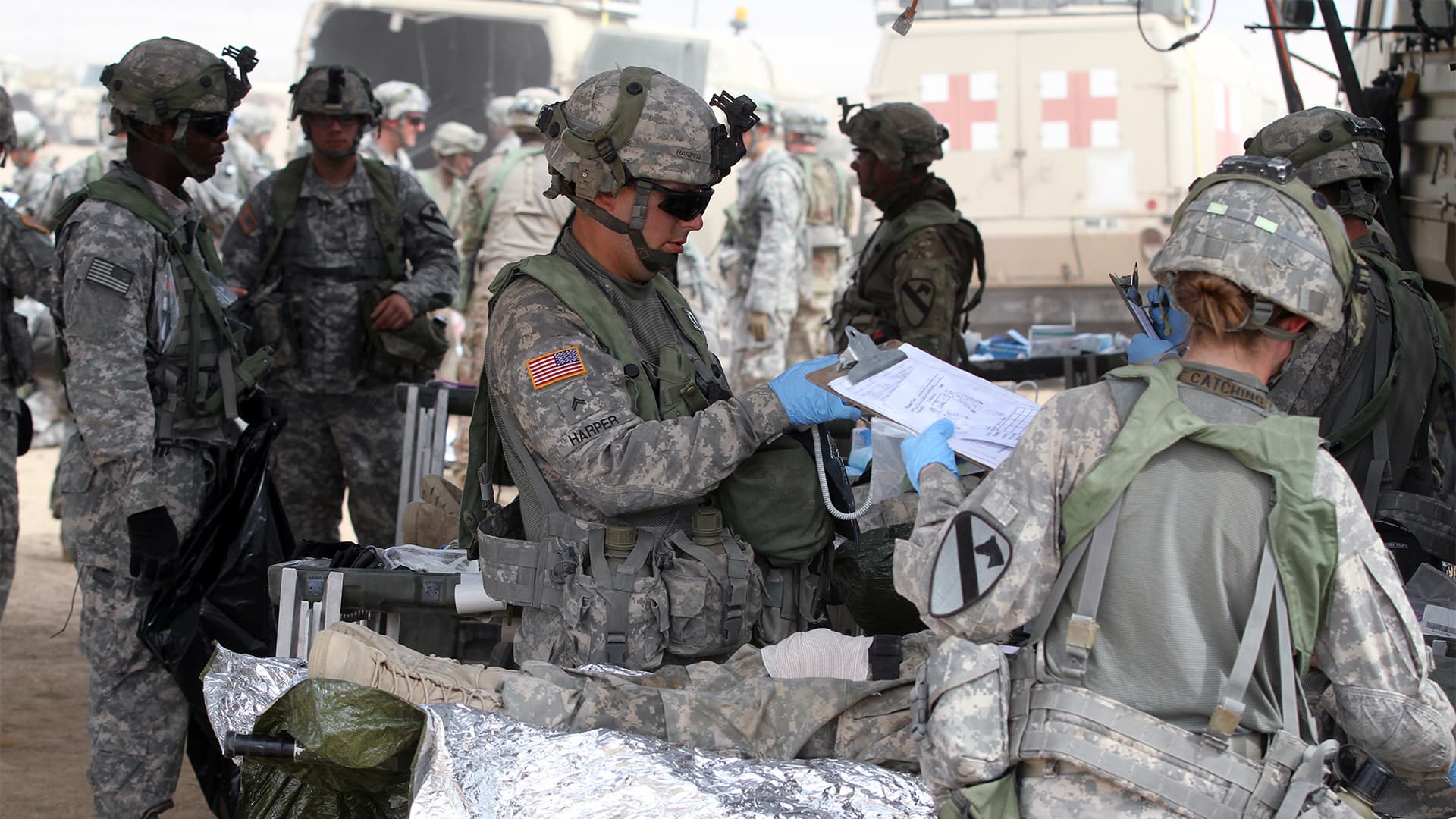 Military personnel in combat gear reviewing documents in a field.